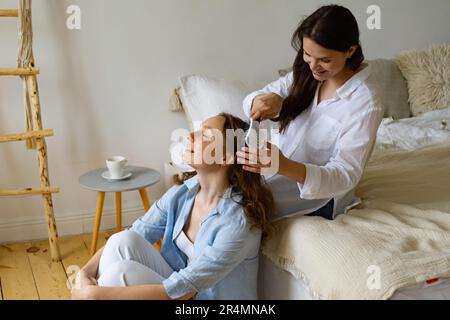 Zwei junge Frauen sitzen zu Hause zusammen, eine putzt dem anderen die Haare Stockfoto