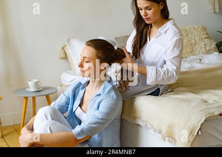 Zwei junge Frauen sitzen zu Hause zusammen, eine putzt dem anderen die Haare Stockfoto