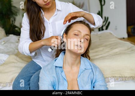 Zwei junge Frauen sitzen zu Hause zusammen, eine putzt dem anderen die Haare Stockfoto