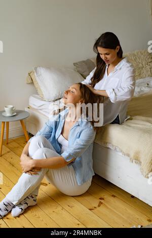 Zwei junge Frauen sitzen zu Hause zusammen, eine putzt dem anderen die Haare Stockfoto