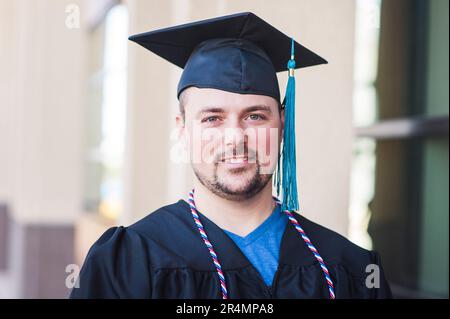 Lächelndes Porträt eines männlichen Absolventen in schwarzer Mütze und schwarzem Kleid Stockfoto