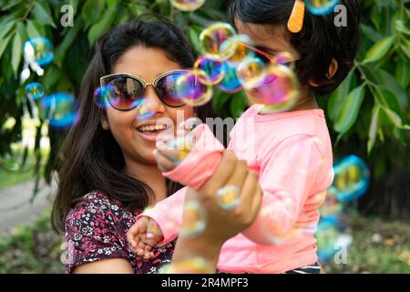 Schwestern spielen und machen Spaß mit Seifenblasen im Freien Stockfoto