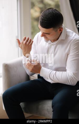 Foto eines Mannes, das den Manschettenknopf am Hemdarm befestigt. Bräutigam-Morgen bei der Hochzeit Stockfoto