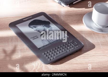 Amazon Kindle eBook Reader auf einem Holztisch neben einer Pflanze und einer Tasse Kaffee. Leerer Kopierbereich für Editortext. Stockfoto