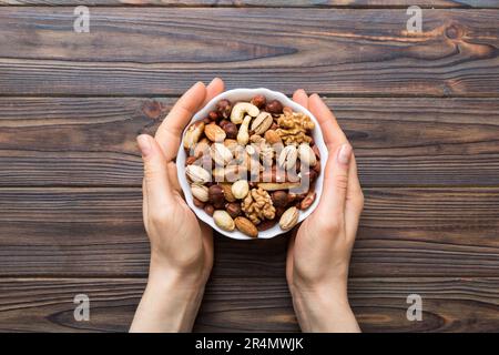 Frauenhände halten eine Holzschüssel mit gemischten Nüssen, Walnuss, Pistazien, Mandeln, Haselnüssen und Cashews. Gesundes Essen und Snack. Vegetarische Snacks dif Stockfoto