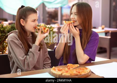 Zwei Teenager essen Pizza im Café draußen nach dem Unterricht. Zwei Freunde Teilen Sich Pizza Stockfoto