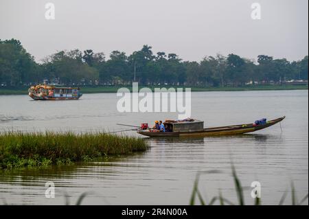 Zwei einheimische Männer sitzen ruhig in ihrem traditionellen engen Fischerboot, während ein Drachenboot am frühen Abend am Perfume River, Hue, Vietnam vorbeifährt. Stockfoto