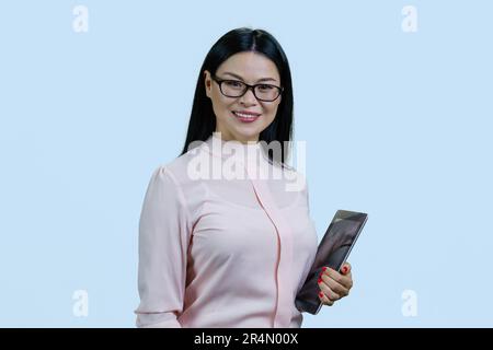 Porträt einer klugen Asiatin in Brille mit Tablet-pc. Isoliert auf blassblauem Hintergrund. Stockfoto