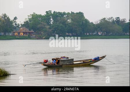 Zwei einheimische Männer sitzen ruhig in ihrem traditionellen engen Fischerboot im frühen Abendlicht auf dem Perfume River, Hue, Vietnam. Stockfoto