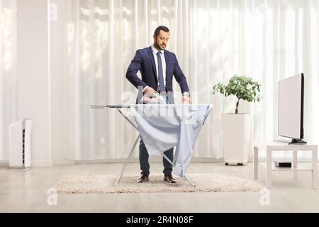 Geschäftsmann bügelt zu Hause ein Hemd vor dem fernseher in einem Wohnzimmer Stockfoto