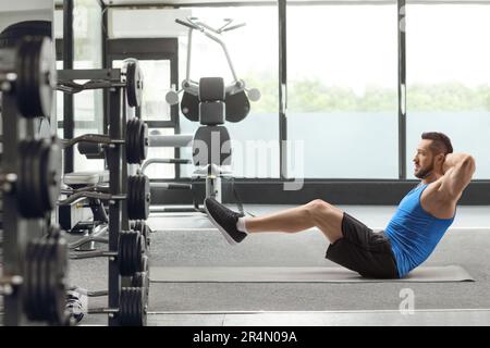 Passender junger Mann, der bauchmuskeln auf einer Matte im Fitnessstudio trägt Stockfoto