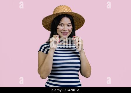 Porträt einer jungen asiatischen Touristenfrau mit Strohhut und Sonnenbrille. Isoliert auf pinkfarbenem Hintergrund. Stockfoto