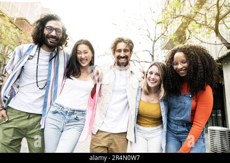 Eine bunte Gruppe von fröhlichen Millennials-Freunden, die sich auf der Straße umarmen. Fröhliche, multiethnische, junge, sorgenfreie Freunde, die lachen und Stockfoto