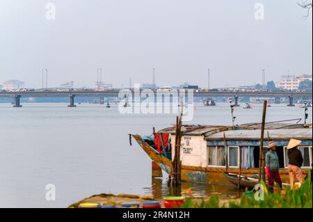 Phu-Xuan-Brücke mit starkem Verkehr über den Parfüm-Fluss mit Booten, die am Flussufer im Vordergrund festgemacht sind. Hue, Vietnam. Stockfoto