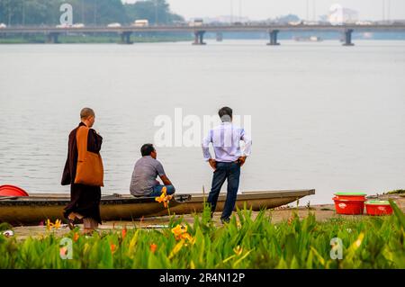 Ein buddhistischer Mönch wandelt von zwei Männern in stiller Unterhaltung und blickt auf den Perfume River im frühen Abendlicht, Hue, Vietnam. Stockfoto