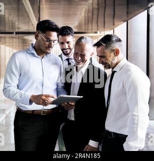 Eine vielseitige Gruppe von Geschäftsleuten, die ein Tablet in einem Büroflur checken. Junge Führungskraft, die ein Gerät in einem Meeting mit Kollegen hält Stockfoto