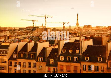 Pariser Stadtbild mit Eiffelturm und Kranichen bei goldenem Sonnenuntergang. Paris, Frankreich. Panoramablick. Städtischer Hintergrund. Stockfoto