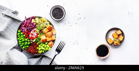 Gesundes veganes Essen. Buddha-Schüssel mit Quinoa, gebratenem Tofu, Avocado, Edamame, grünen Erbsen, Rettich, Kohl und Sesamsamen. Weißer Küchentisch mit Backgroun Stockfoto