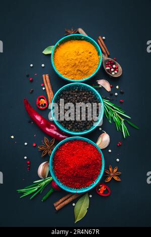 Gewürze und Gewürze zum Kochen auf dunklem Hintergrund. Paprika, Kurkuma, Pfefferkörner und andere. Flach liegend, Draufsicht. Stockfoto