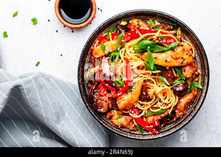 Gebratene Nudeln mit Hähnchen, roter Paprika, Pilzen, Schnittlauch und Sesamsamen in der Schüssel umrühren. Asiatische Küche. Weißer Tischhintergrund, Draufsicht Stockfoto