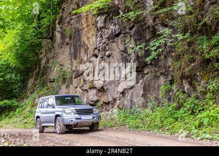 Geländewagen mit Geländewagen auf einer Schotterstraße mit vertikalen Steinklippen, die mit Bäumen und Moos überwuchert sind, Straße zum Zekari Pass (Meskheti Range), Georgia Stockfoto