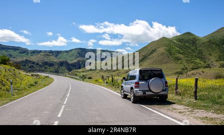 Geländewagen im Geländewagen auf einer Asphaltstraße im Mtkvari-Flusstal in der Samtskhe Javakheti-Region in Südgeorgien, grüne Graslandschaften und Kaukasusberge. Stockfoto