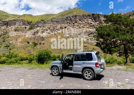 Geländewagen mit Geländewagen auf einer Schotterstraße, im Hintergrund befindet sich der Klosterkomplex Vardzia Cave, Georgia. Stockfoto