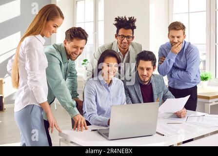 Lächelndes Team von Mitarbeitern, die gemeinsam einen Laptop-Bildschirm betrachten Stockfoto