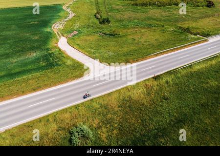 Luftaufnahme eines Radfahrers, der an einem sonnigen Sommertag auf der Asphaltstraße durch die Landschaft fährt, Drone pov High Angle View Stockfoto