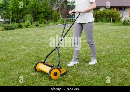 Junge Frau, die mit einem Rasenmäher mit manuellem Druck Rasen mäht Stockfoto