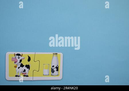 Informationspuzzles am Rand des blauen Hintergrunds. Milch und Kuh in einem Glas. Stockfoto