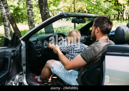 Papa zeigt seinem kleinen Sohn, wie er das Auto fährt, während er hinter dem Steuer sitzt Stockfoto