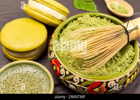 Bambus-Schneebesen in einer Schüssel mit Matcha-Pulver. Grüner Matcha-Tee und Makkaroni-Kuchen. Schließen Stockfoto