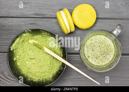 Zwei Makkaroni-Kuchen und eine Tasse Matcha-grünen Tee. Messlöffel in Schüssel mit Matcha-Pulver. Dunkler Holzhintergrund. Stockfoto