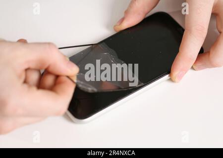 Der Mann entfernt das alte zerbrochene Schutzglas aus dem Telefon. Zerbrochenes Schutzglas Stockfoto