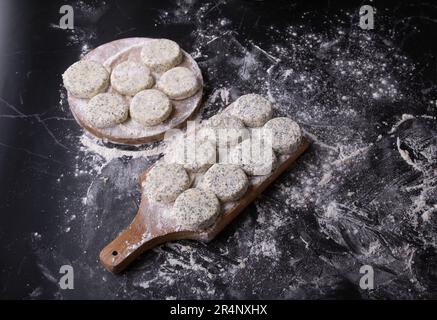 Fotografieren Sie runde Käsekuchen mit Mohnsamen auf Holzbrettern in Mehl, Hüttenkäse als Dessert Stockfoto