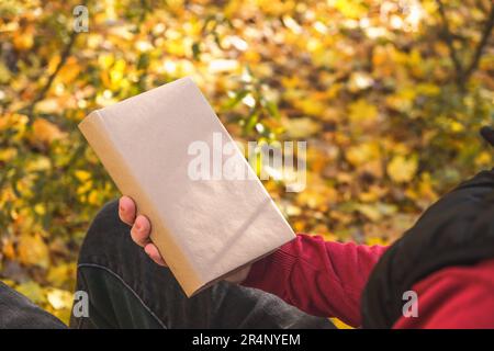 Ein Mann hält ein Buch mit leerem Raum in der herbstlichen Natur. Platz für Buchkopien. Das Konzept des Lesens von Büchern in der Natur. Freier Raum für Werbung. Stockfoto