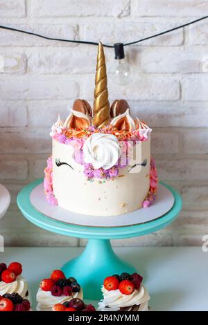 Einhornkuchen mit goldenem Horn, Buttercreme, Makronen und Baiser auf weißem Hintergrund Stockfoto