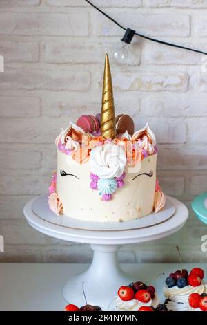 Einhornkuchen mit goldenem Horn, Buttercreme, Makronen und Baiser auf weißem Hintergrund Stockfoto