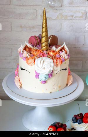 Einhornkuchen mit goldenem Horn, Buttercreme, Makronen und Baiser auf weißem Hintergrund Stockfoto