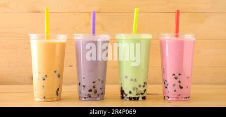 Plastikbecher mit verschiedenen leckeren Bubble Tea auf Holzhintergrund Stockfoto