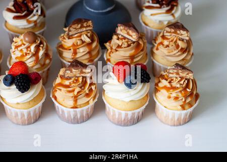 Gesalzene Karamell-Cupcakes mit Schokoladenbissen und Vanille-Cupcakes mit frischen Beeren Stockfoto