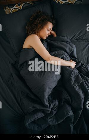 Junge Frau schläft in fetaler Position auf einem ergonomischen Bett Stockfoto