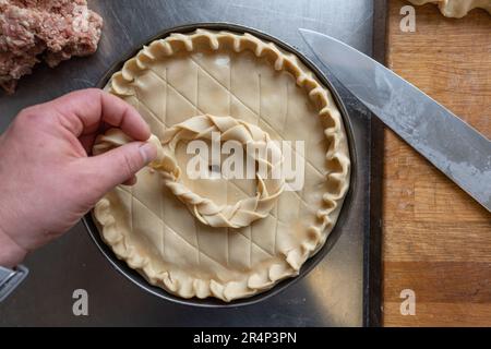 Die traditionelle Pork Pie wird auf einem Tisch aus Metall abgerundet, mit Küchenchef. Stockfoto