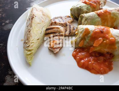 Kohlbrötchen mit saftig gegrilltem Schweinefilet, serviert neben gekochtem Kohl und einer lebhaften Tomatensoße, elegant auf makellosem Boden angeordnet Stockfoto