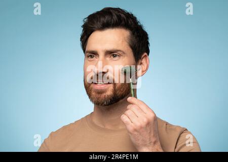 Routineverfahren und kosmetische Kurbehandlungen. Gutaussehender Mann mittleren Alters mit Gesichtswalze zur Anti-Aging-Hautbehandlung Stockfoto