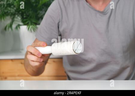 Der Typ entfernt Haare und Wolle vom T-Shirt mit einem Fusselroller. Ein Mann mit einer Haarentfernungswalze. Stockfoto