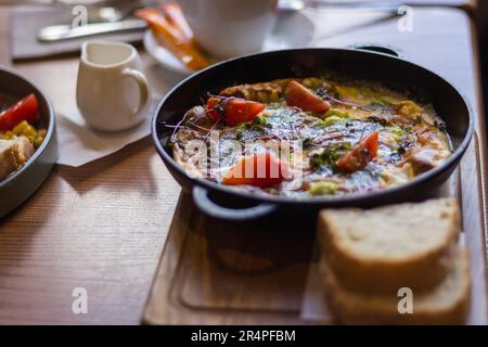 Spiegeleier mit Tomaten und Schinken in der Pfanne. Frühstückstisch serviert. Omelette mit Tomaten und Brot. Spanische Tortilla. Eier mit Pesto und Gemüse. Stockfoto