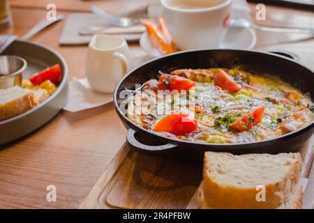 Spiegeleier mit Tomaten und Schinken in der Pfanne. Frühstückstisch serviert. Omelette mit Tomaten und Brot. Spanische Tortilla. Eier mit Pesto und Gemüse. Stockfoto