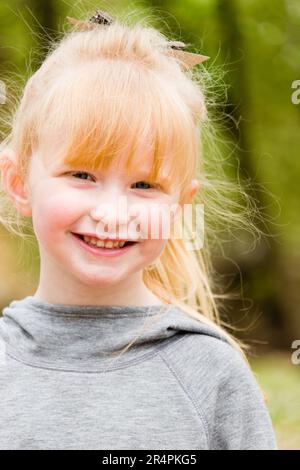 Porträt eines lächelnden blonden Weißen Mädchens mit grauem Oberteil. Stockfoto